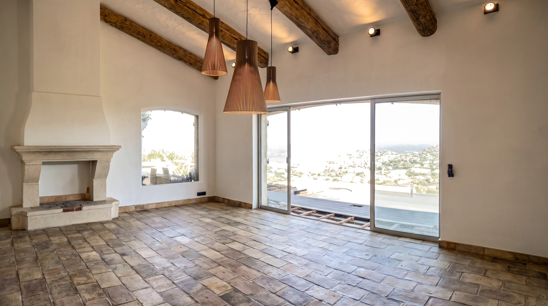 Salon vide, haut plafond avec poutres apparentes en bois brut, sol en carreaux de terre cuite ancienne